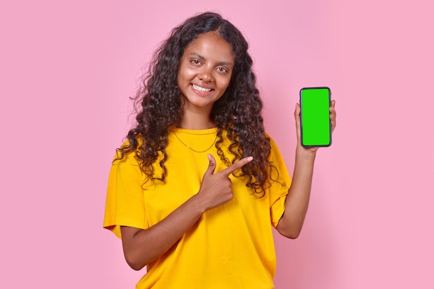 Young smiling indian woman teen points finger at phone stands in studio