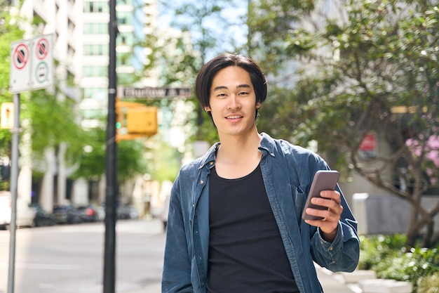 Photo young smiling japanese man holding smartphone using mobile app looking camera communication online