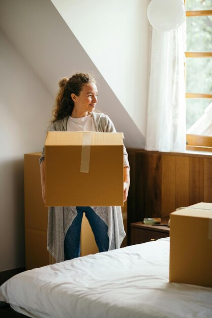 カジュアルな服を着た笑顔の若い女性が手に大きな紙箱を持って立ち近くを見送っています