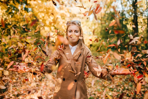 Foglie di autunno di lancio sorridenti di giovane signora su in parco soleggiato