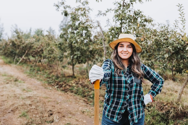 Young smiling latin peasant woman using gardening gloves and leaning on a shovel