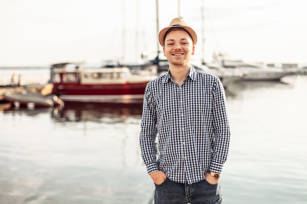 Foto giovane maschio sorridente con cappello e camicia sullo sfondo dello yacht club