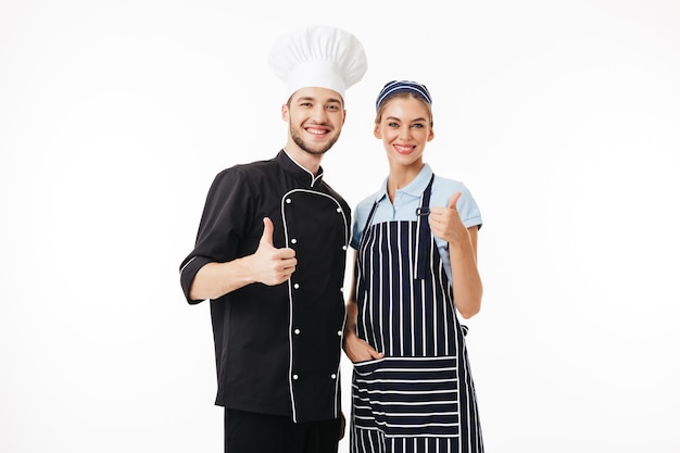 검은 색 유니폼과 흰색 모자에 젊은 웃는 남자 요리사와 예쁜 여자가 행복하게 스트라이프 앞치마와 모자 요리