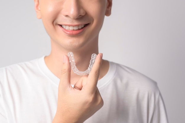 흰색 배경 스튜디오 위에 invisalign 교정기를 들고 웃는 젊은 남자