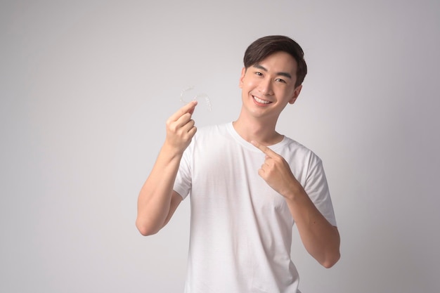 Young smiling man holding invisalign braces over white background studio