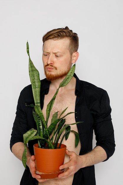 A young smiling man holds in his hands a small flower on white background.