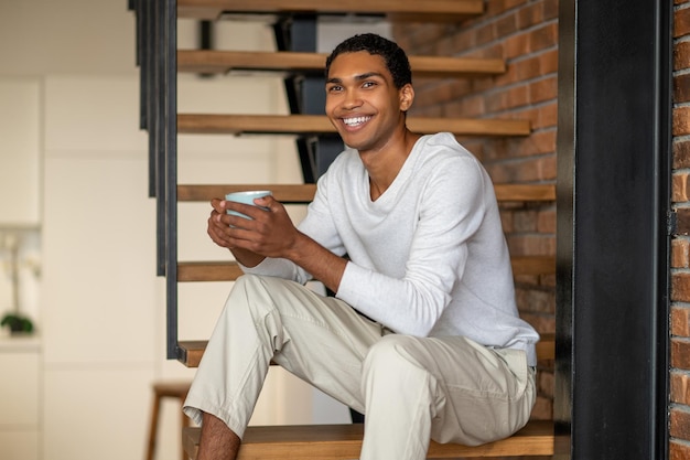 Young smiling man at home having coffee and looking contented