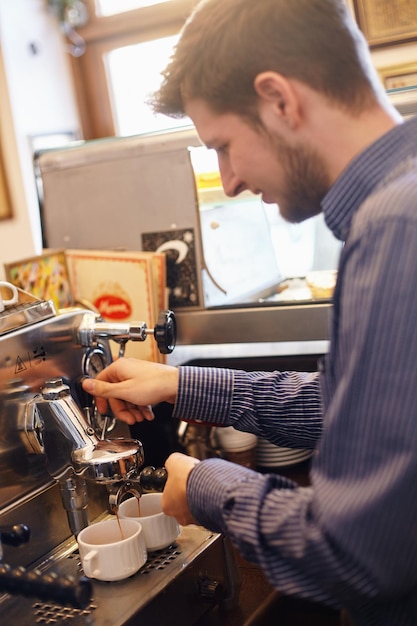 웃고 있는 젊은 남자가 커피 머신으로 커피를 만들고 있다.