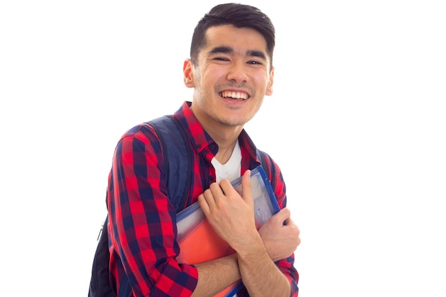 파란색 배낭과 카피북이 있는 폴더가 있는 빨간색 체크 무늬 셔츠를 입은 웃고 있는 젊은 남자