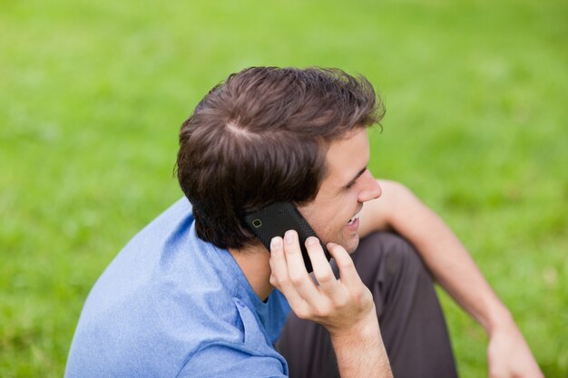 Молодой улыбающийся человек, разговариваете по телефону, сидя в парке