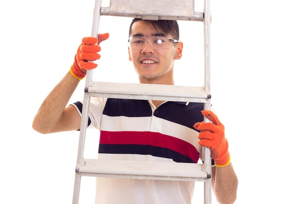 Young smiling man in white and tshirt with orange gloves and protective glasses holding the ledder