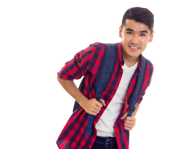 Young smiling man with black hair in jeans white Tshirt and red checkered shirt with blue backpack