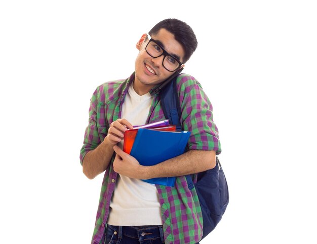 Young smiling man with black hair in Tshirt and checkered shirt with blue backpack holding books