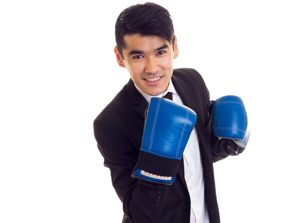 Giovane uomo sorridente con capelli neri in camicia bianca e smoking nero con cravatta e guanti da boxe blu