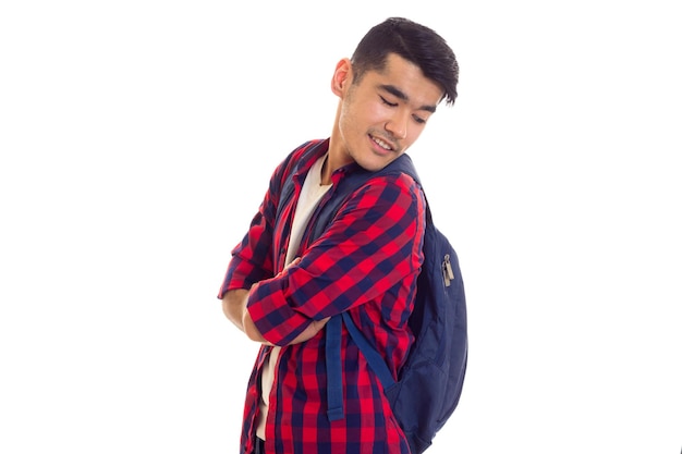 Young smiling man with black hair in white Tshirt and red checkered shirt looking at his backpack