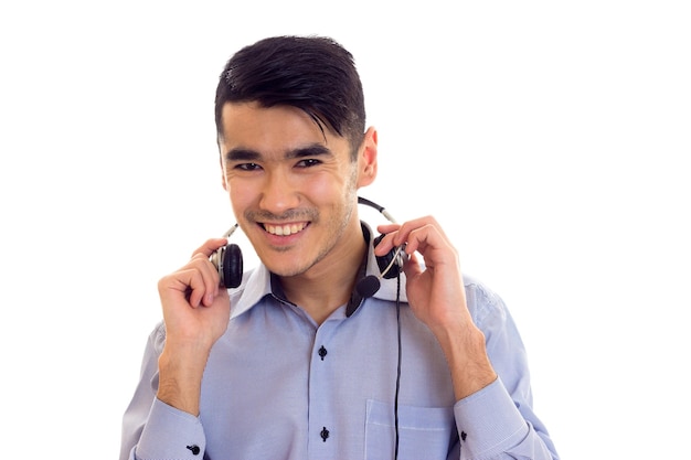 Young smiling man with dark hair in blue shirt with black headphones on white background in studio