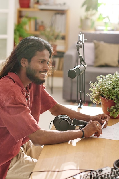 Young smiling man with dark long hair communicating with guest\
in studio