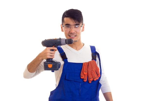 Young smiling man with orange gloves and protective glasses holding electric screwdriver