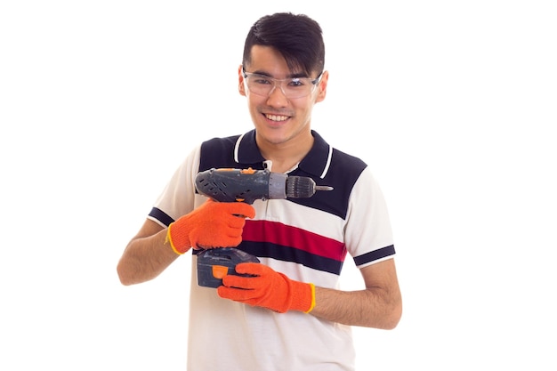 Young smiling man with orange gloves and protective glasses holding grey electric screwdriver