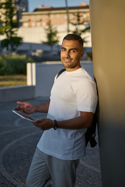 Young smiling middle eastern man using digital tablet looking at camera on the street