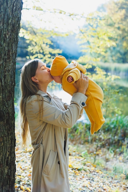 Young smiling mother holding her little son in her arms while standing in a sunny park A walk with a newborn baby in nature