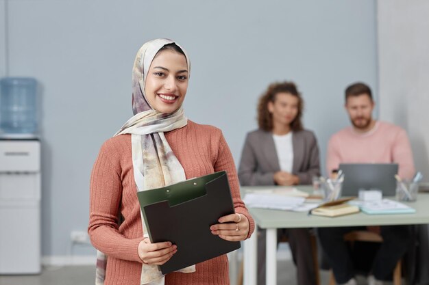 Young smiling multiethnic female business leader with folder looking at you