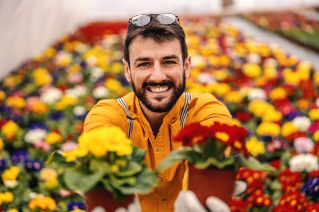 Foto giovane operaio sorridente del vivaio che dà i vasi con i fiori