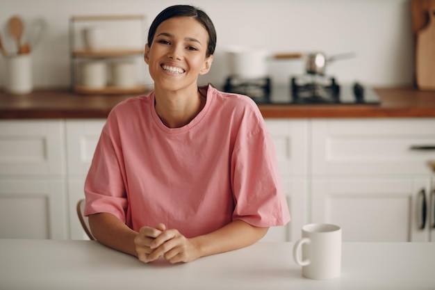 A young smiling positive woman is sitting in the kitchen