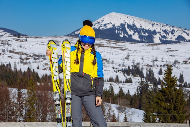 Young smiling pretty woman holding ski. mountains on background. winter travel. copy space