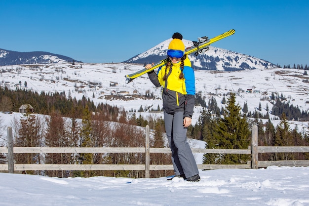 Young smiling pretty woman holding ski. mountains on\
background. winter travel