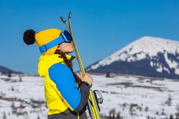 Young smiling pretty woman holding ski mountains on background