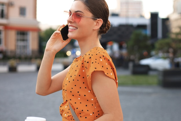 Photo young smiling pretty woman talking by phone, walking on the street.