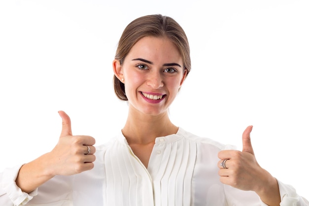 Young smiling pretty woman in white blouse showing thumbs up on white background in studio