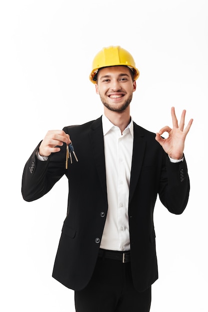 Young smiling realtor in yellow safety helmet showing ok gesture happily 