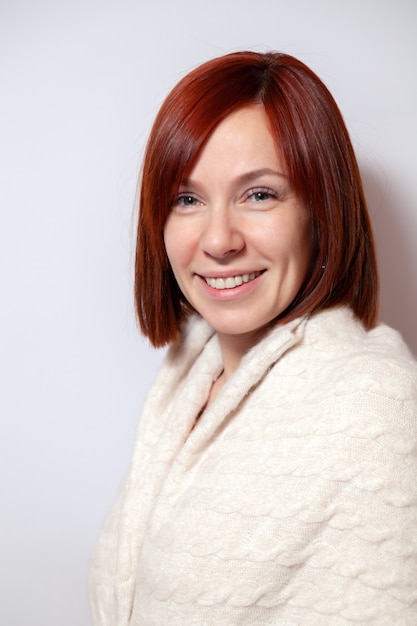 Young smiling red haired woman in knitted beige sweater