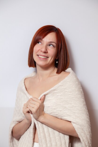 Young smiling red haired woman in knitted beige sweater