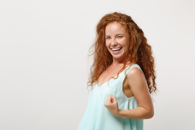 Giovane ragazza sorridente della donna della testarossa in vestiti leggeri casuali che posano isolato sul fondo bianco della parete in studio. concetto di stile di vita di emozioni sincere della gente. mock up copia spazio. pugno serrato come vincitore.