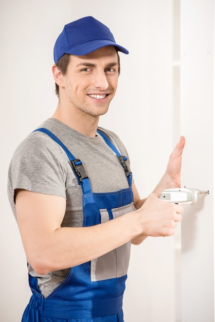 Young smiling repairman using hand drill at home interior.