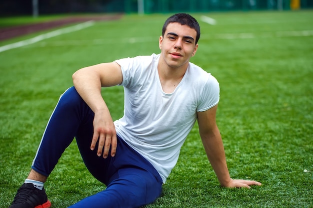 Молодой усмехаясь спортсмен сидя на траве