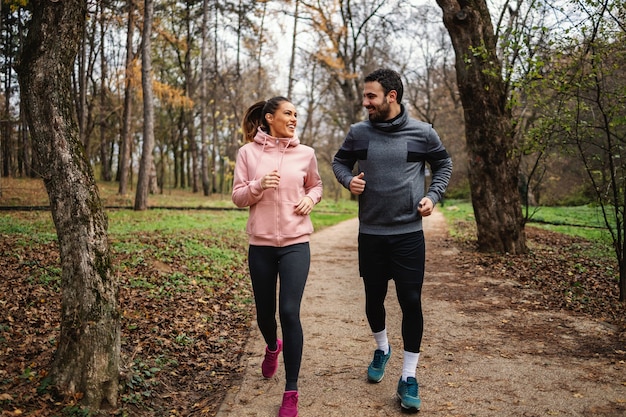 秋の森の中を走り、マラソンの準備をしている健康的な習慣を持つ若い笑顔のスポーツウーマン。