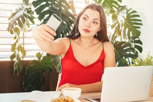 Giovane ragazza sorridente dello studente che fa selfie con il suo smartphone mentre sul lavoro