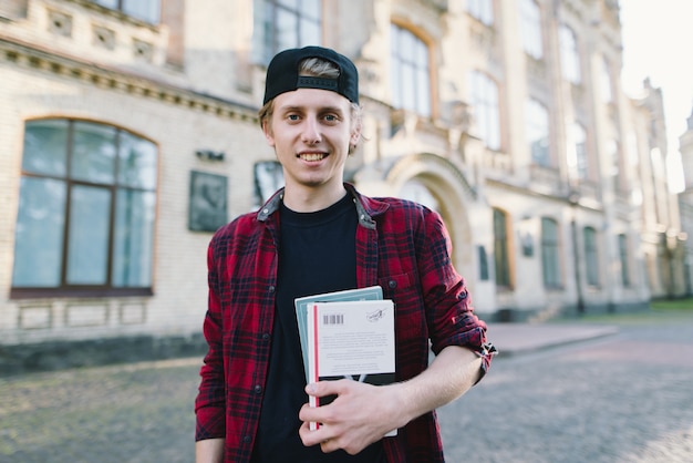 Foto giovane studente sorridente in una camicia con libri e quaderni nelle mani di un campus universitario. buona vita studentesca. vivere dopo le lezioni. cortile della scuola