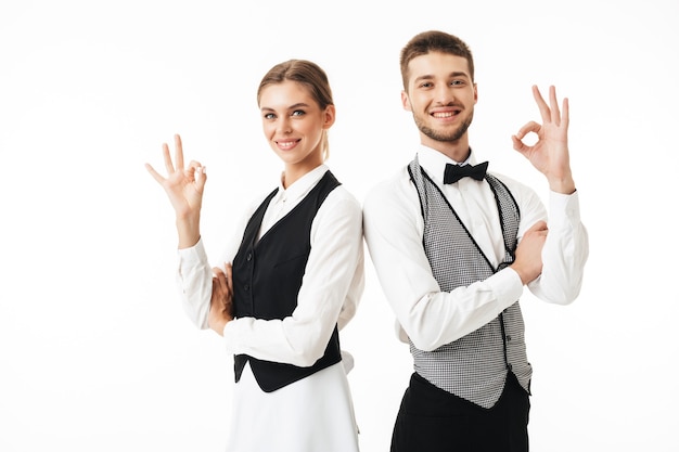 Photo young smiling waiter and waitress in white shirts and vests sstanding back to back happily