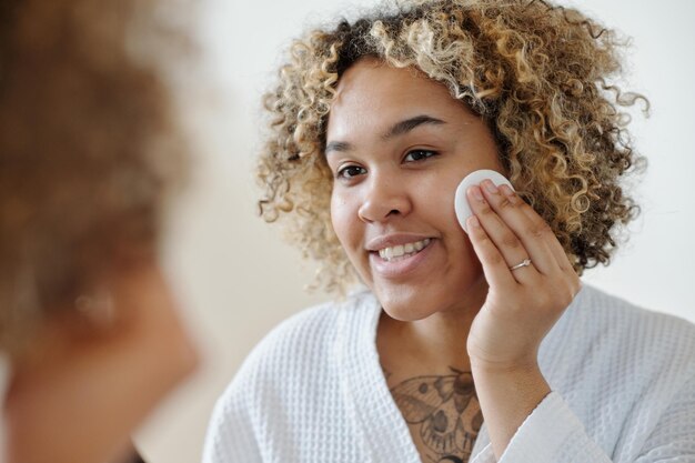 Young smiling woman applying makeup remover with cotton pad