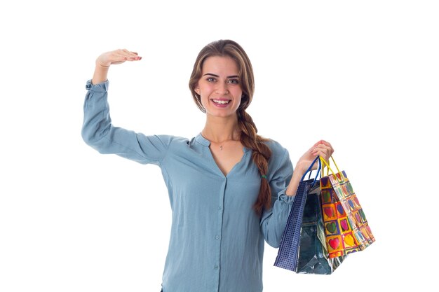 Молодая улыбающаяся женщина в синей блузке держит разноцветные сумки и указывает вниз в студии