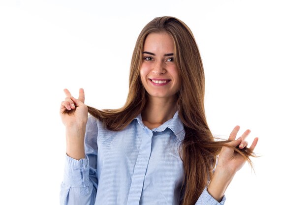 Young smiling woman in blue shirt holding her long brown  hair on white background in studio