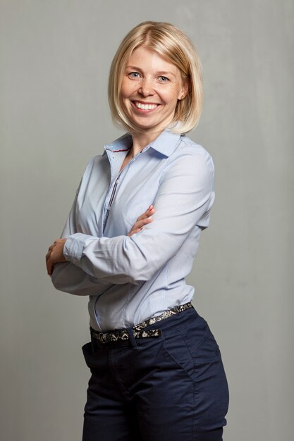 Young smiling woman in a blue shirt and trousers. Business success. Gray wall. Vertical.