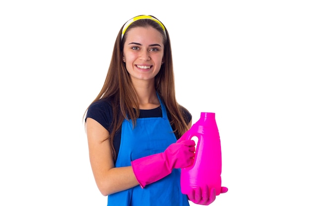 Young smiling woman in blue Tshirt and apron with pink gloves holding detergent in studio
