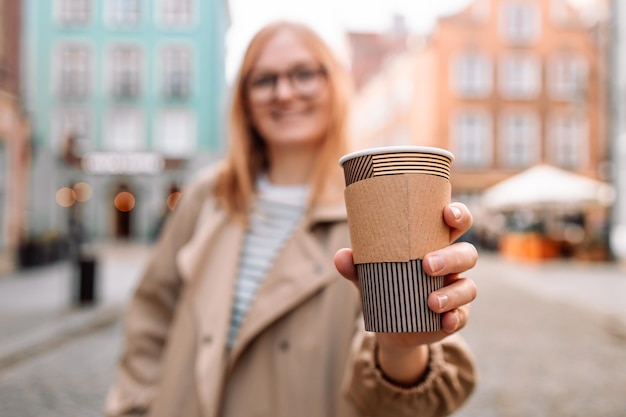 Young smiling woman in coat with coffee cup in evening city street in gdansk old town traveling euro