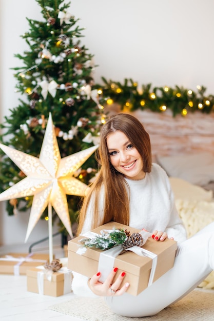 贈り物とクリスマスツリーで飾られたリビングルームで若い笑顔の女性